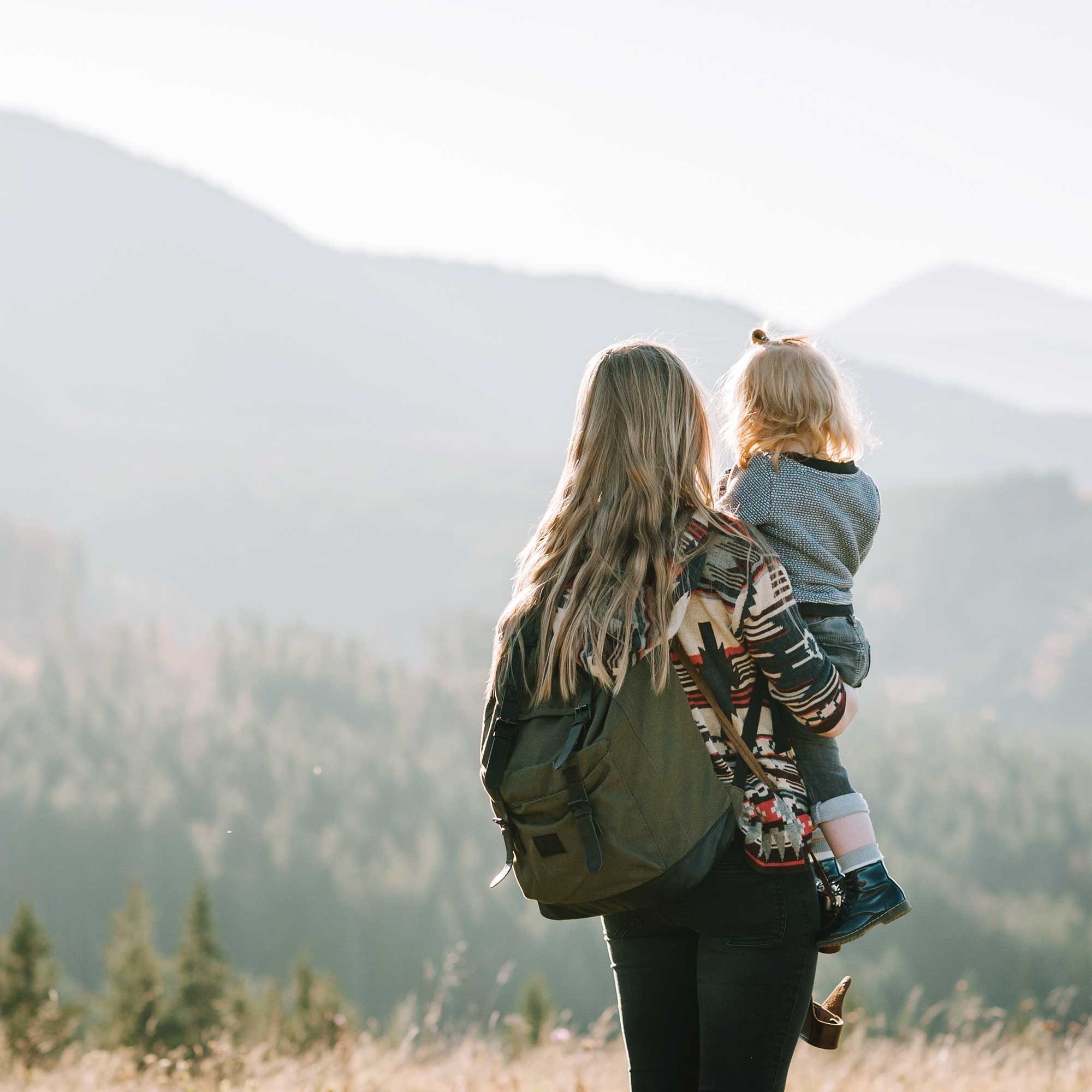 Woman with backpack on holding small child looking at the mountains