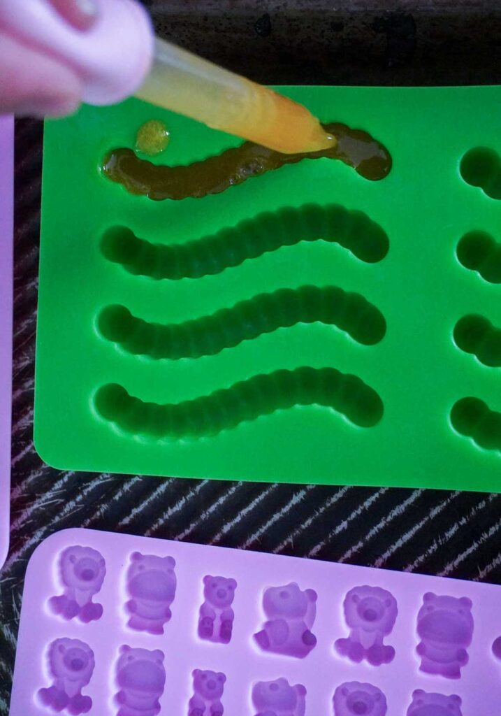 close up of pink dropper putting orange juice into silicon gummy worm mold