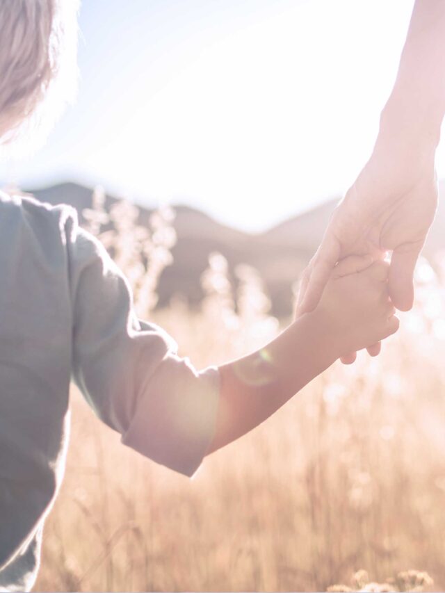 child holding mom's hand in a field of wheat.