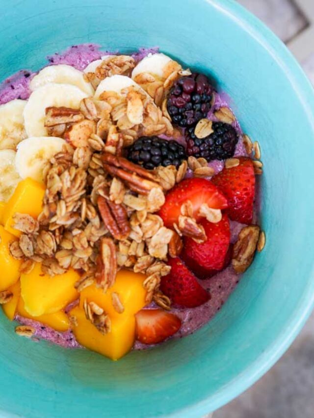 top view of protein smoothie bowl with fruit and granola on top, in a green glass bowl