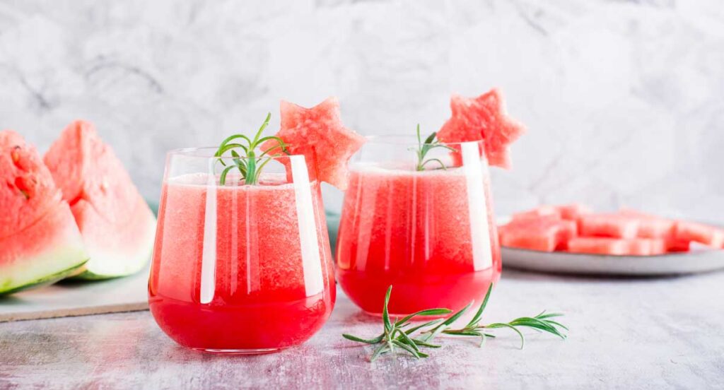 two glasses of fresh watermelon juice  in front of a cut watermelon.