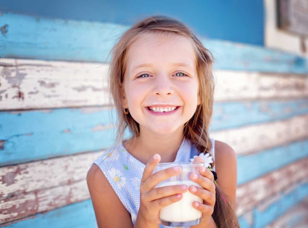 small girl smiling and drinking a glass of raw milk