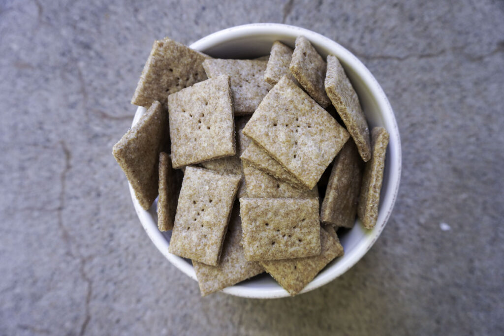 white bowl of whole wheat sourdough crackers on a concrete countertop
