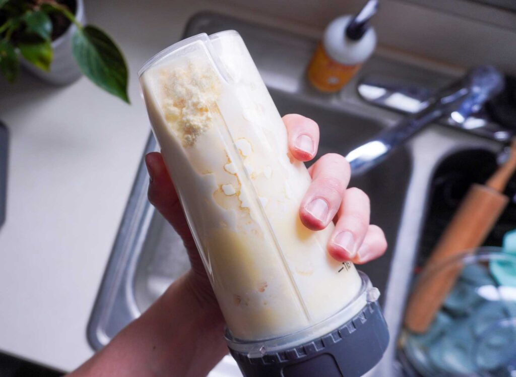 hand holding a plastic ninja blender cup with homemade butter separating inside