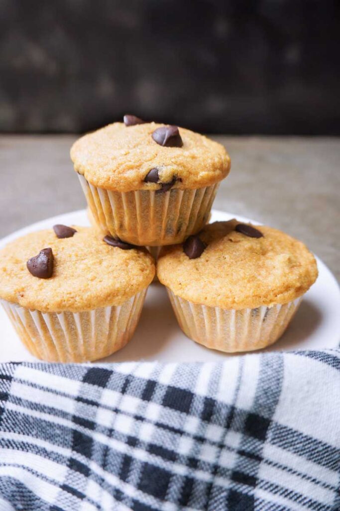 vertical image of three chocolate chip fresh milled flour healthy muffins stacked on a plate