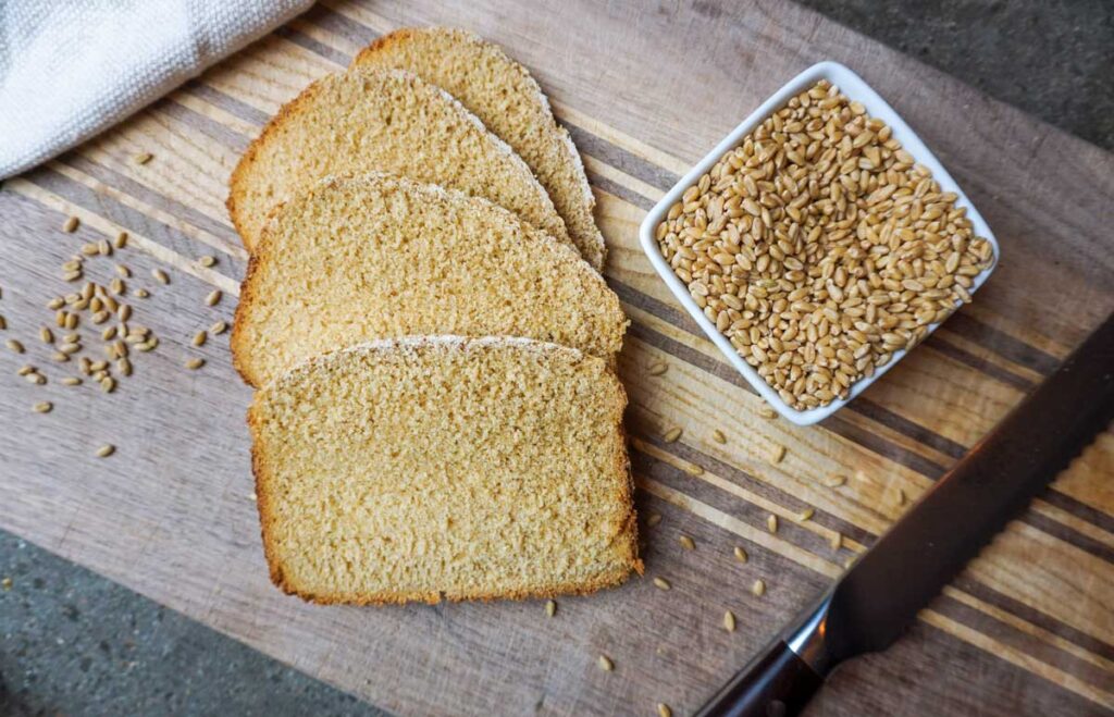 Four slices of fresh baked bread on a wooden cutting board with a bread knife.