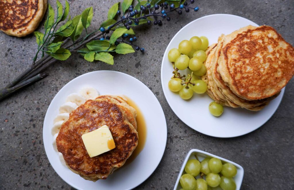 Top view of breakfast pancakes on white plates with grapes