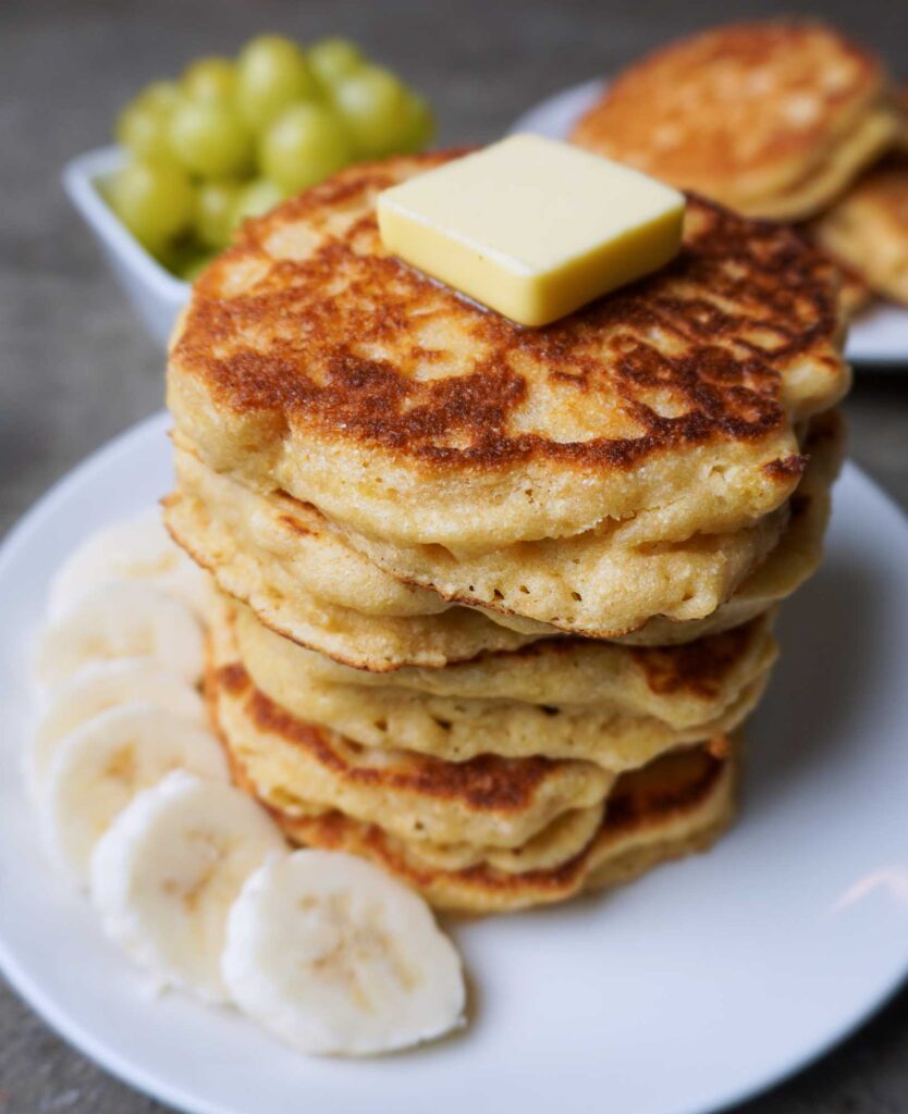 Close up vertical image of a stack of fluffy fresh milled flour pancakes with banana slices.