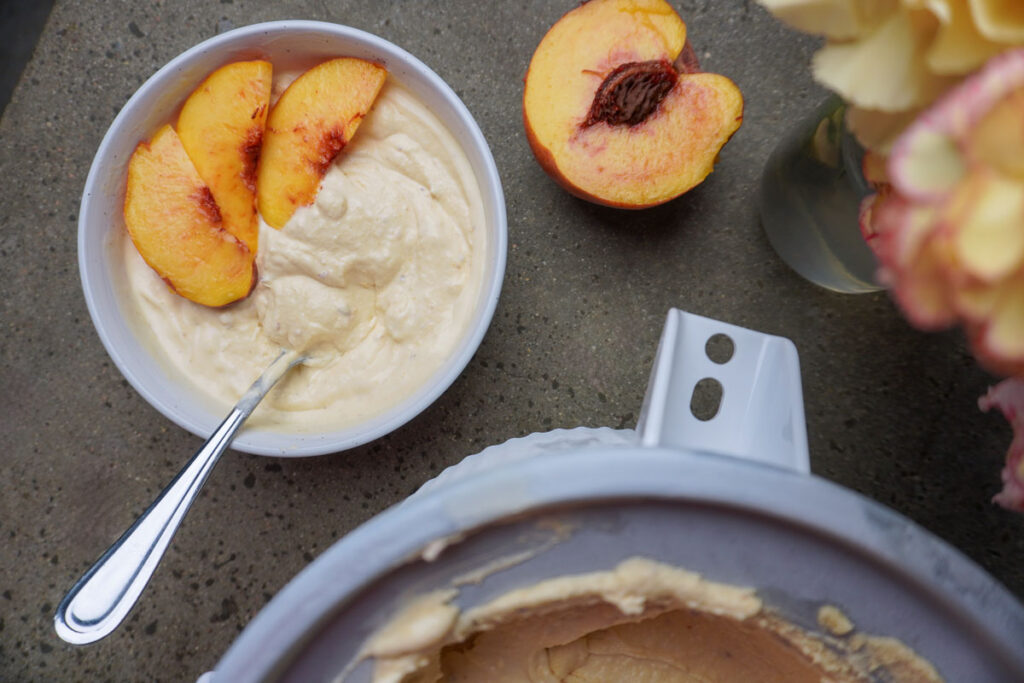 Top view of a bowl of fresh ice cream with fresh peaches on top and a cut open peach