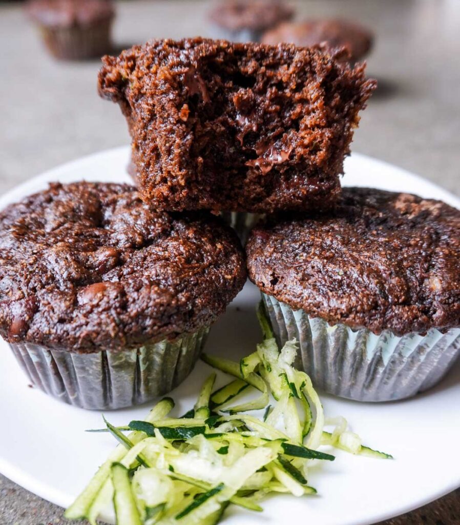 Close up view of three chocolate zucchini muffins with a bite taken out.