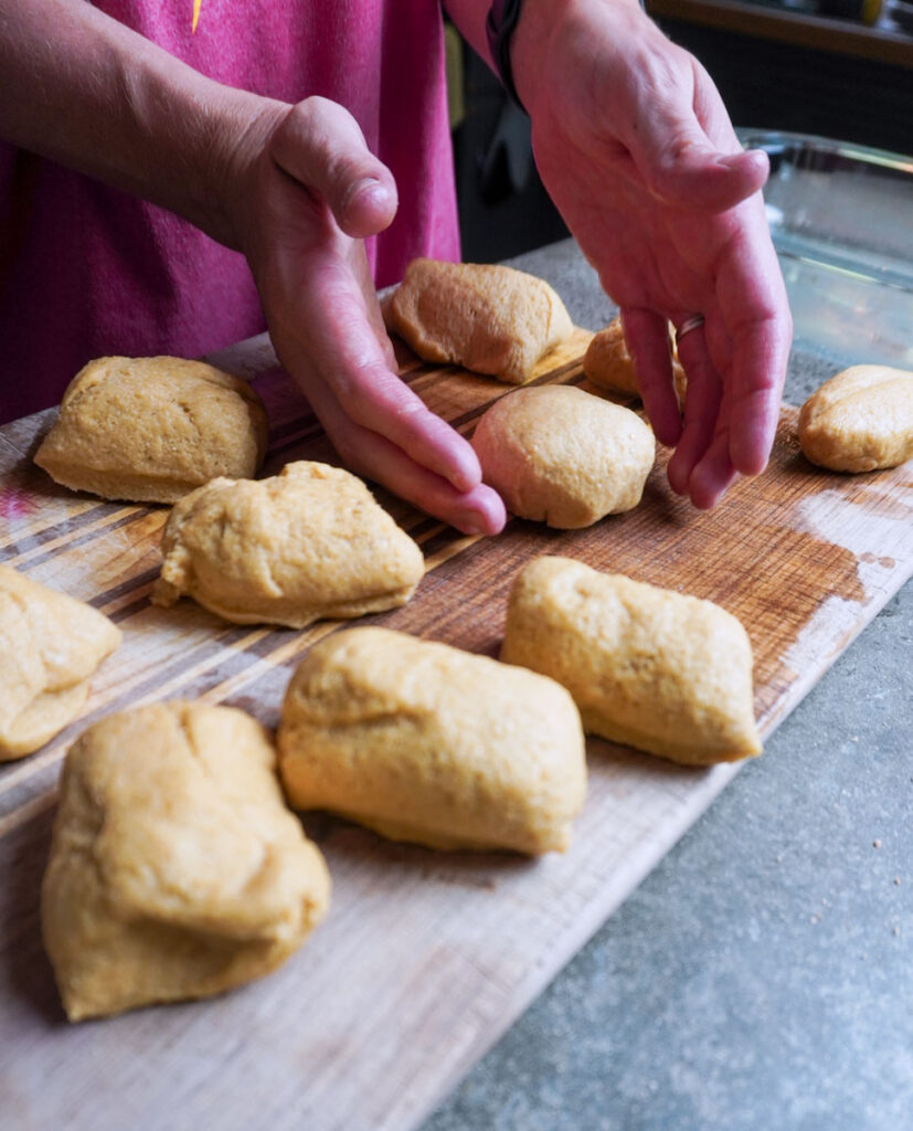 hands shaping several dough balls into dinner rolls