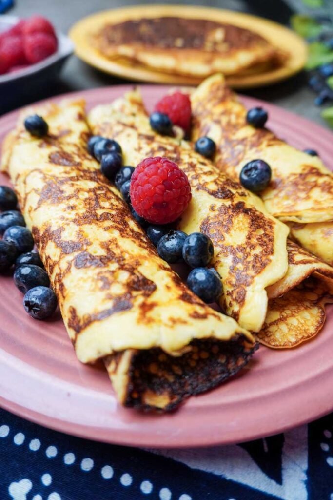 Close up vertical image of three rolled up sourdough crepes with fruit