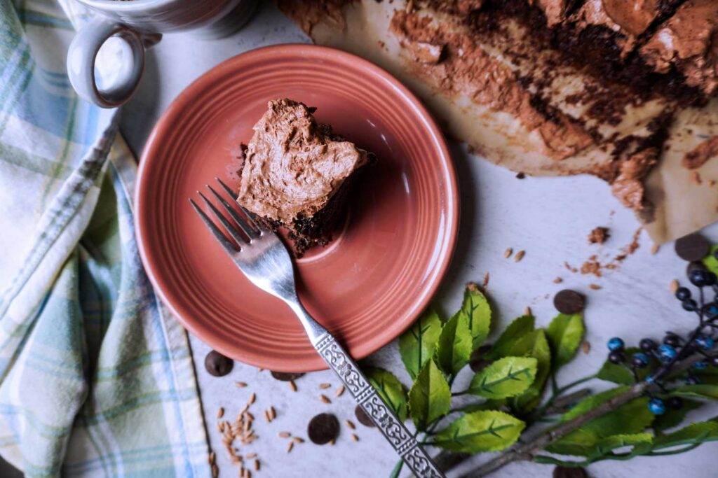 A slice of fresh milled spelt brownie on a pink plate with a fork.