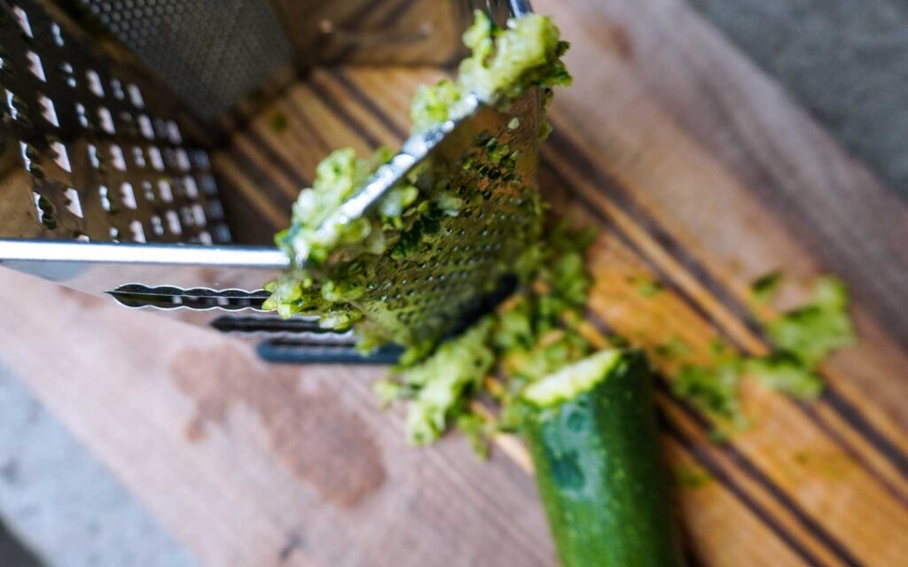Top view of a fresh garden zucchini partially shredded on a cutting board. 