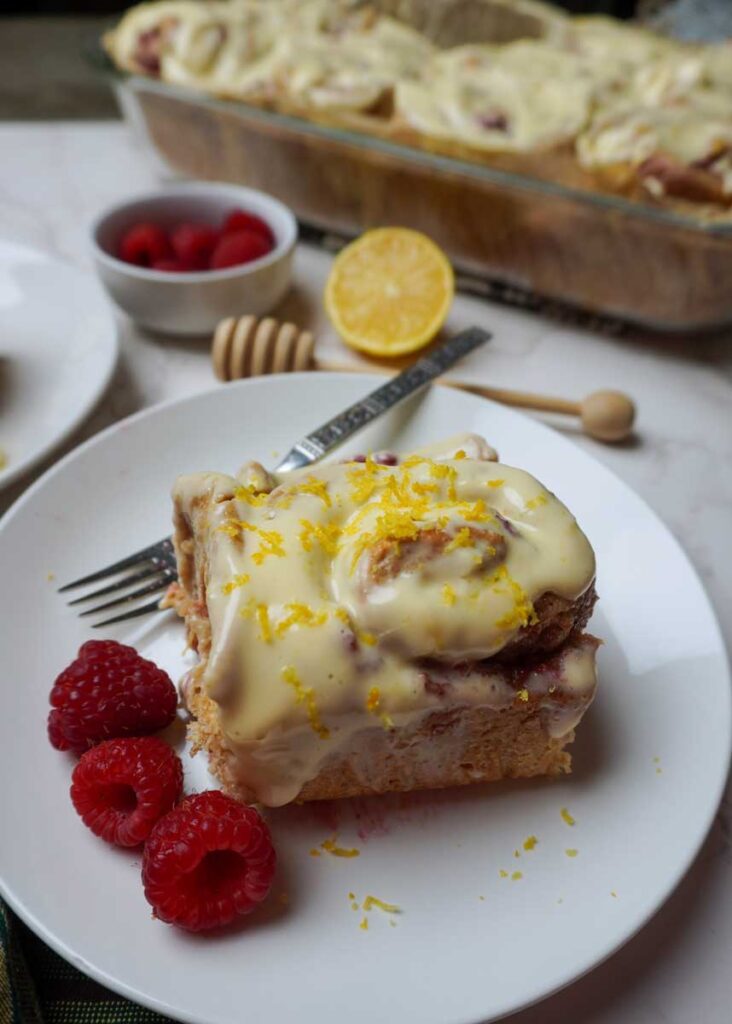 Vertical image of a lemon raspberry roll with lemon zest on top and fresh raspberries.