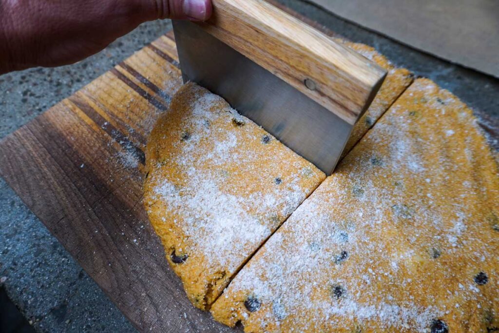 Hand holding a bench scraper and cutting pumpkin scone dough