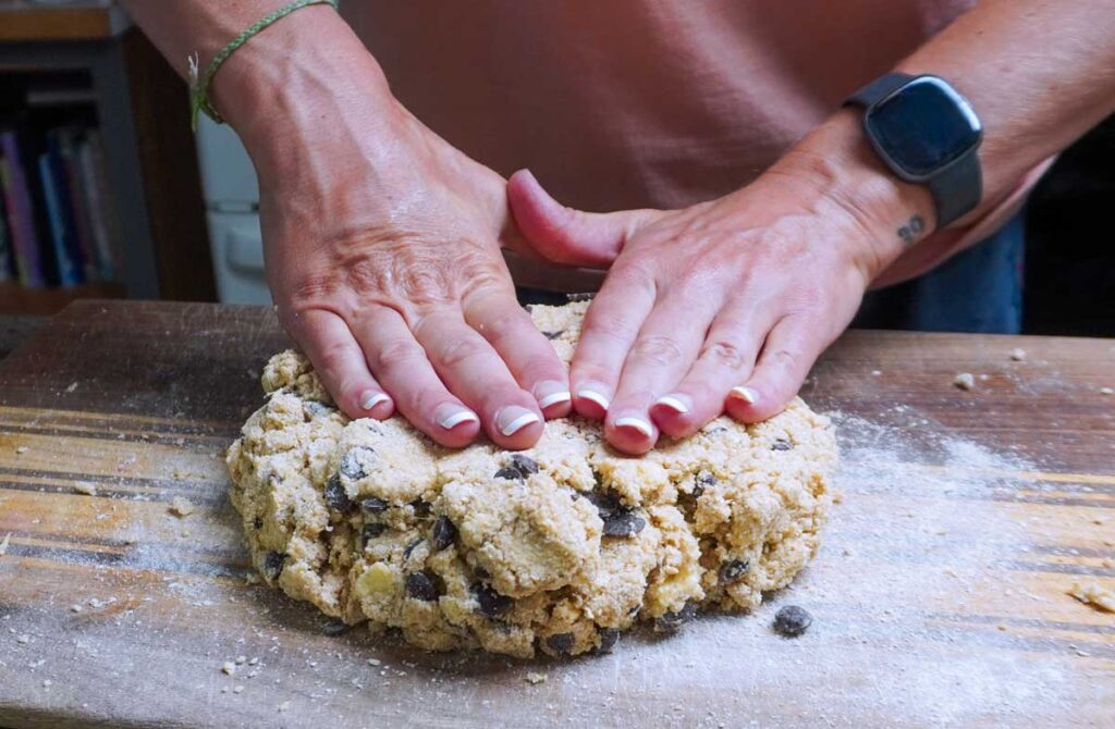 Hands pressing a large ball of sourdough scone dough onto a cuttting board