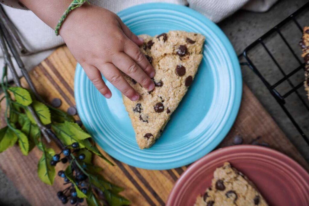 small hand reaching for a chocolate chip scone.