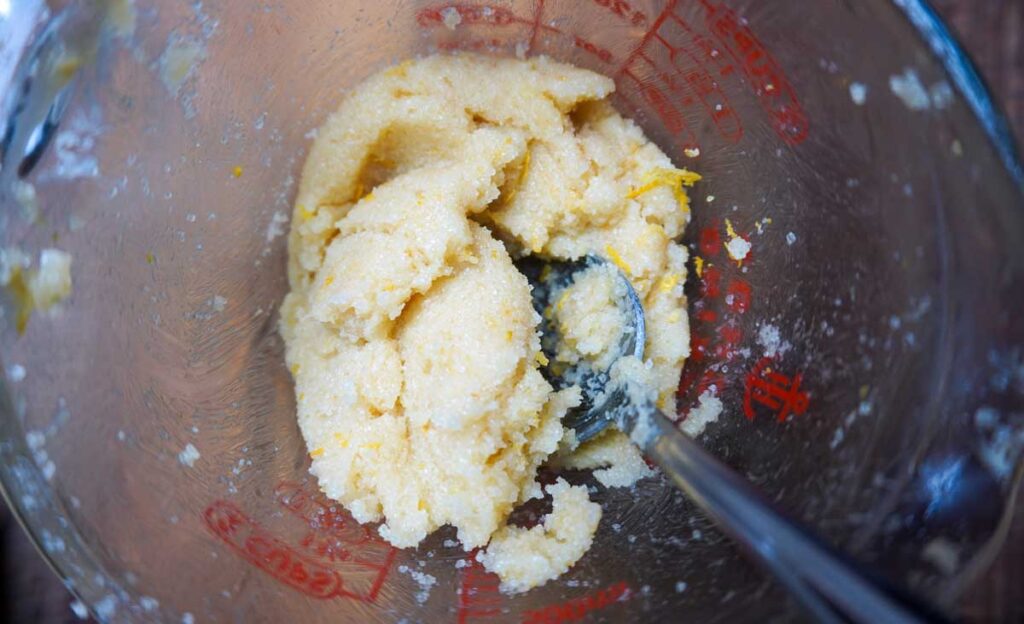 Glass cup with sugar, lemon zest, and butter mixed together and a spoon.