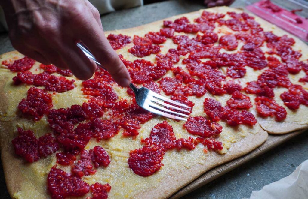 Hand mashing fresh raspberries on top of lemon rolls dough.